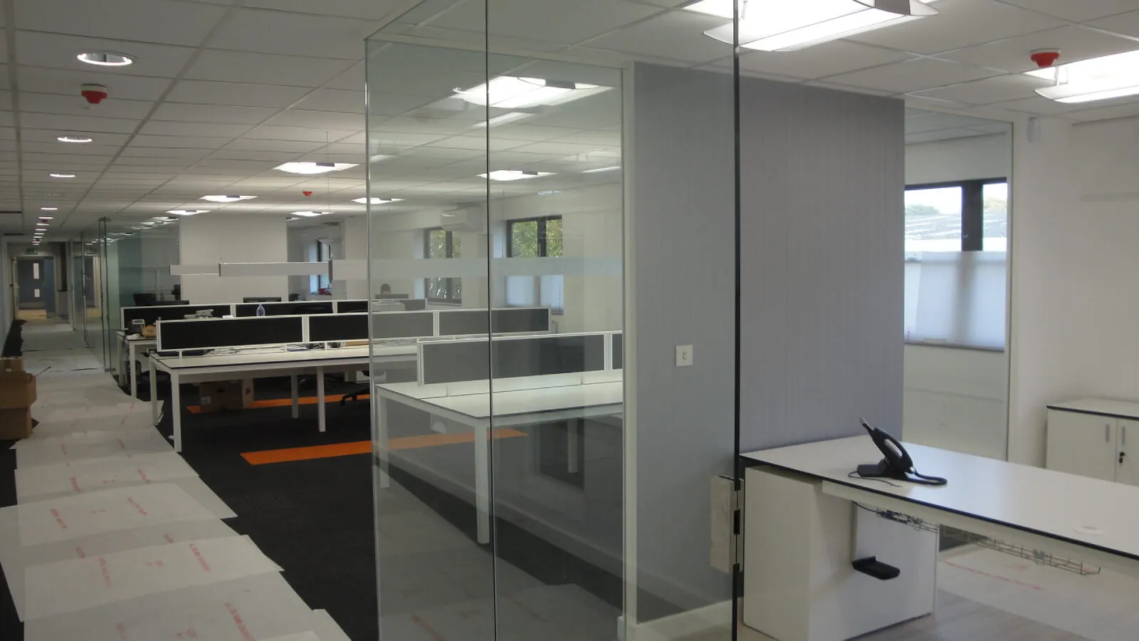 Tansales office space with designer furnitures and carpet tile flooring and suspended grid ceiling and frameless glass partitions screen