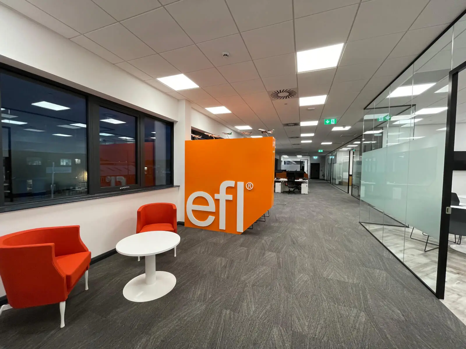 EFL office space with designer back to back desks, chairs, laminated wood flooring, suspended grid ceiling and glass partitions 1