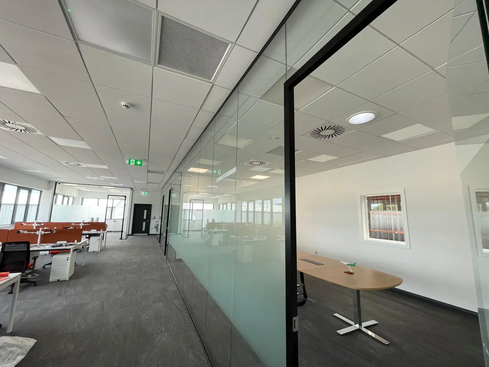 EFL office space with designer back to back desks, chairs, laminated wood flooring, suspended grid ceiling and glass partitions 15