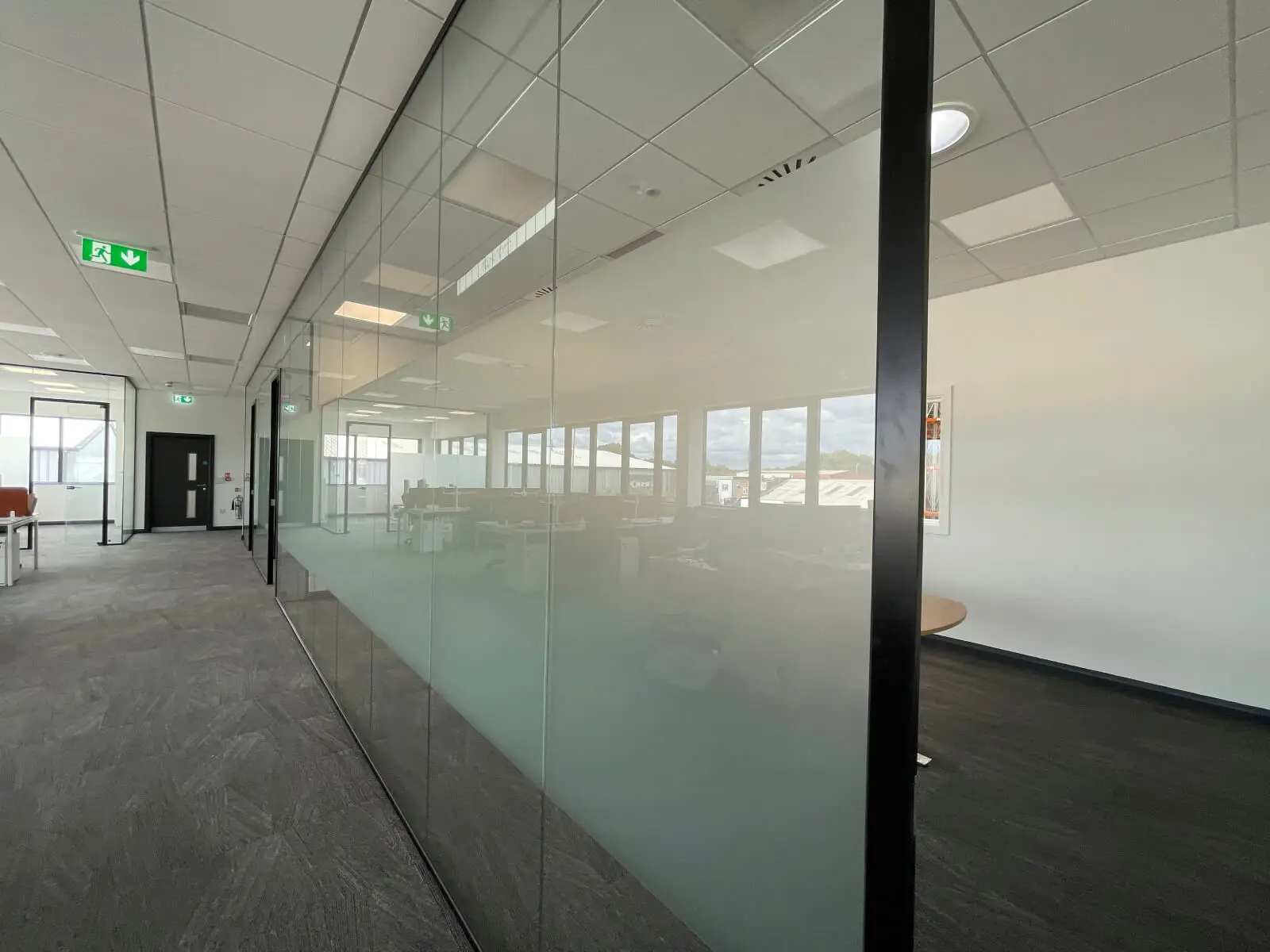 EFL office space with designer back to back desks, chairs, laminated wood flooring, suspended grid ceiling and glass partitions 16