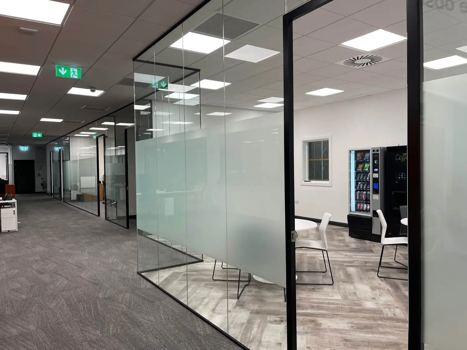 EFL office space with designer back to back desks, chairs, laminated wood flooring, suspended grid ceiling and glass partitions 2