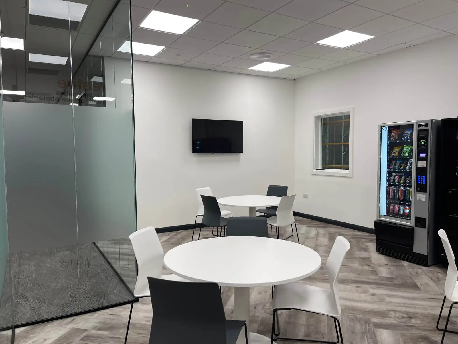 EFL office space with designer back to back desks, chairs, laminated wood flooring, suspended grid ceiling and glass partitions 3