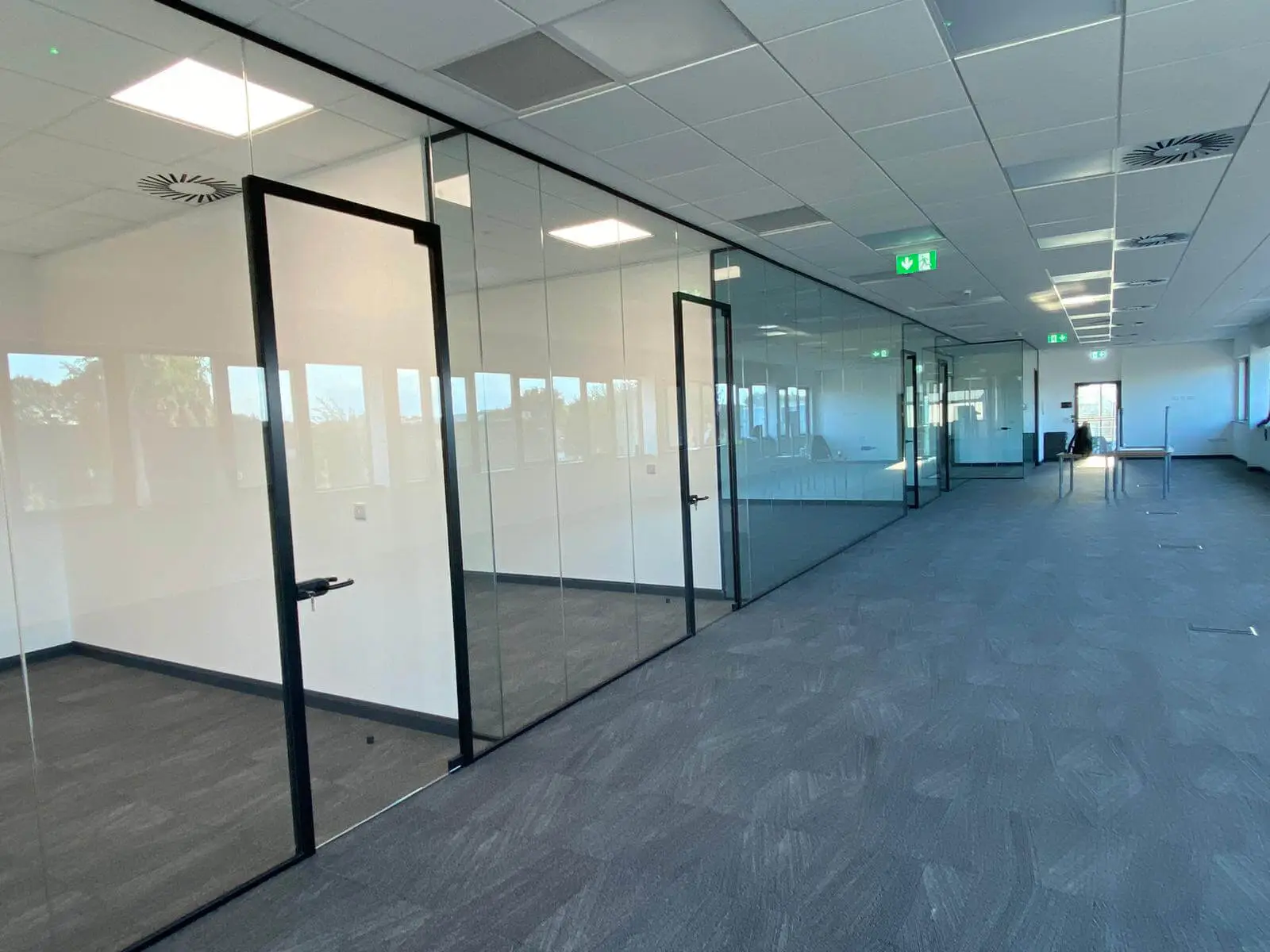 EFL office space with designer back to back desks, chairs, laminated wood flooring, suspended grid ceiling and glass partitions 38