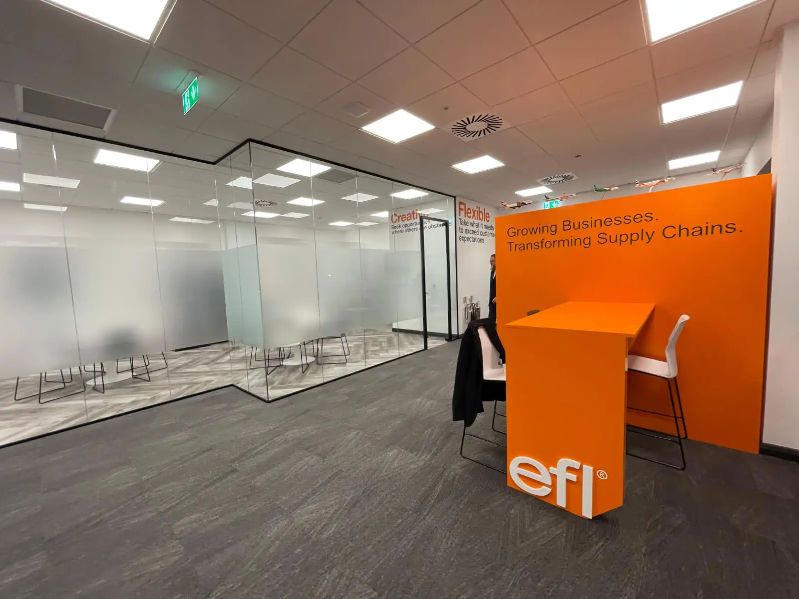 EFL office space with designer back to back desks, chairs, laminated wood flooring, suspended grid ceiling and glass partitions 4